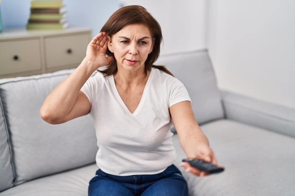 Vrouw met tv-afstandsbediening en hand achter het oor