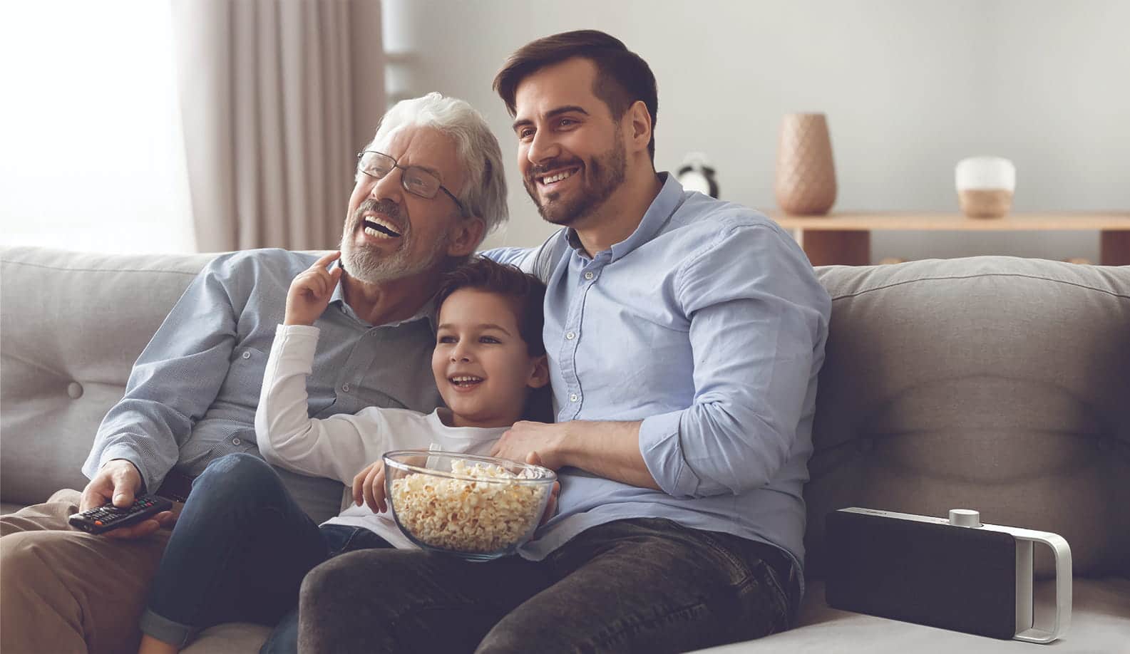 Familie sitzt auf dem Sofa und guckt lachend TV